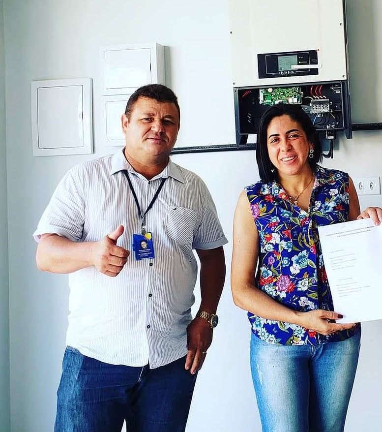 Cliente e técnico da D'Luz diante do inversor recém-instalado, com o contrato em mãos