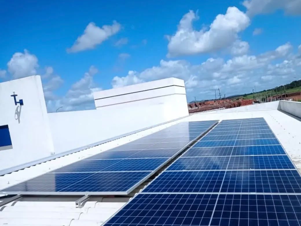 Fileiras de painéis solares instaladas num telhado comercial branco, sob céu azul